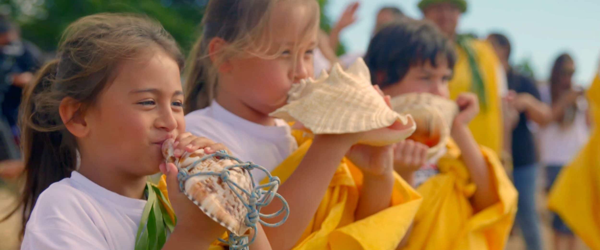 Hawaiian children blowing into conch shells