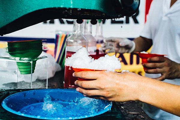 Shave ice machine processing ice into a cup being held by a hand
