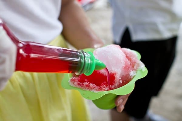 Hand pouring red colored flavoring onto a cup of shave ice