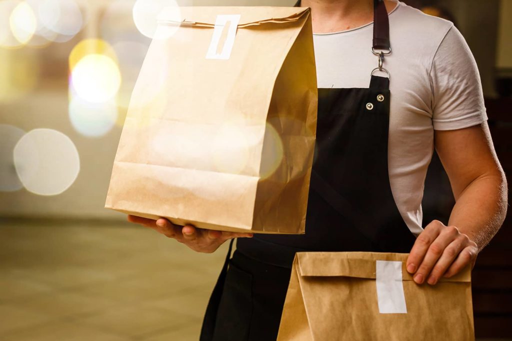 Man wearing a black apron holding food delivery bags