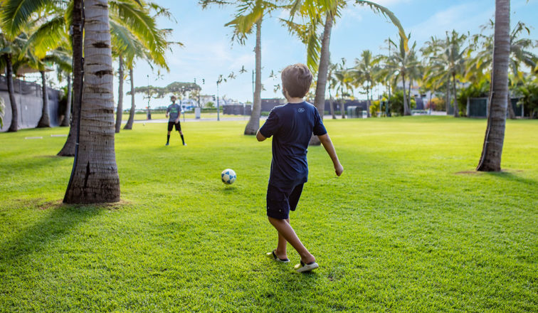 Boys playing soccer in the park under palm trees