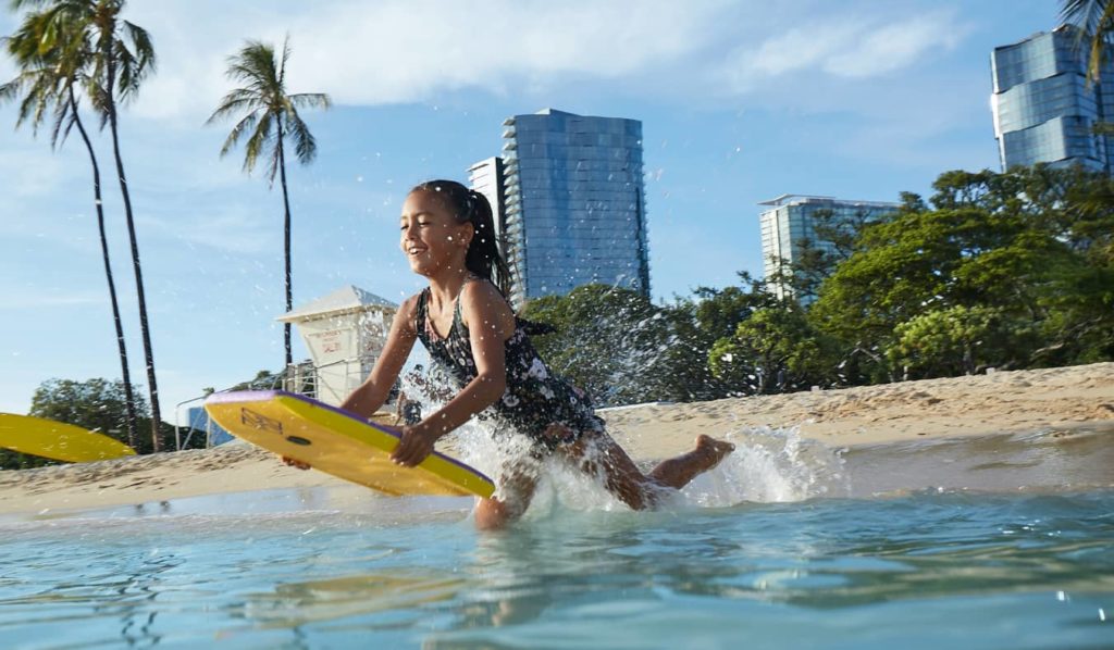 Young girl jumping into the ocean with a yellow boogie board