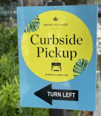Bright blue and yellow Ward Village curbside pickup sign with a black arrow pointing left