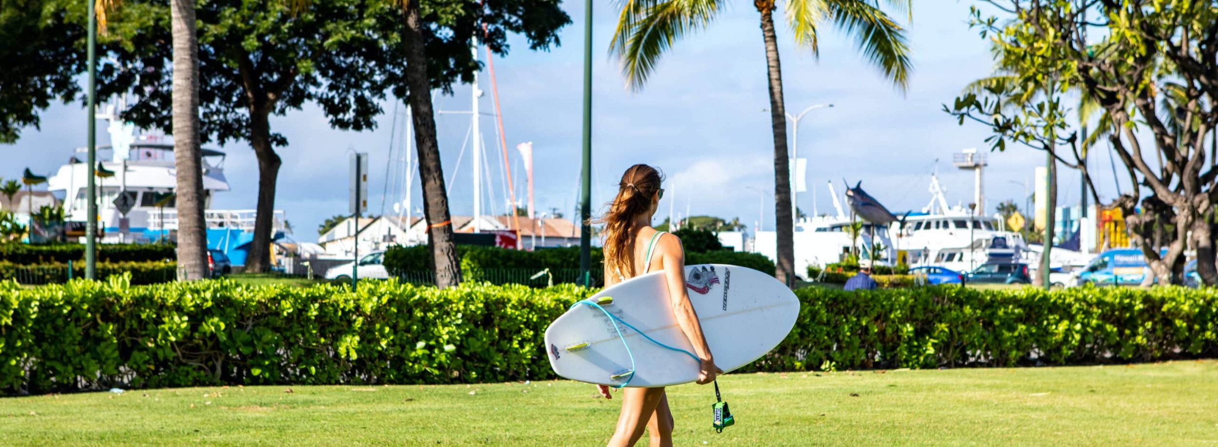 Woman holding surfboard walking through the park