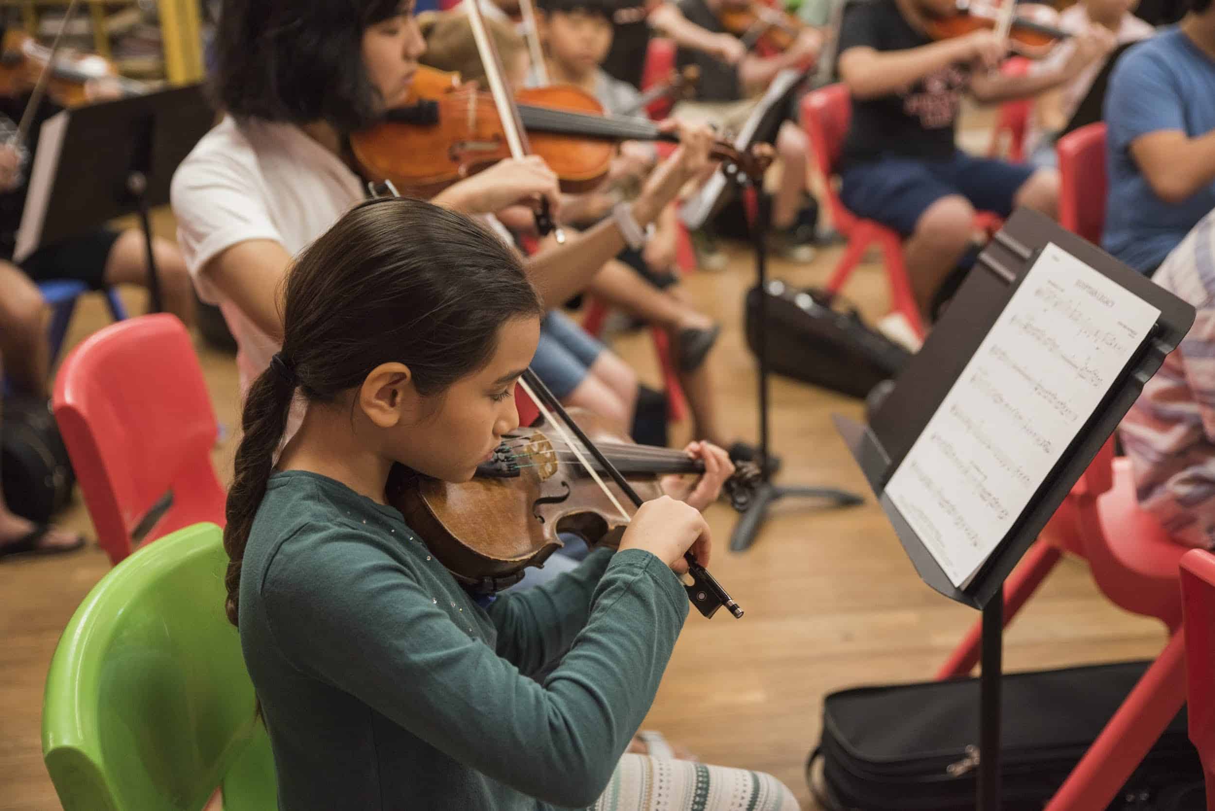 A girl playing the violin with an orchestra.