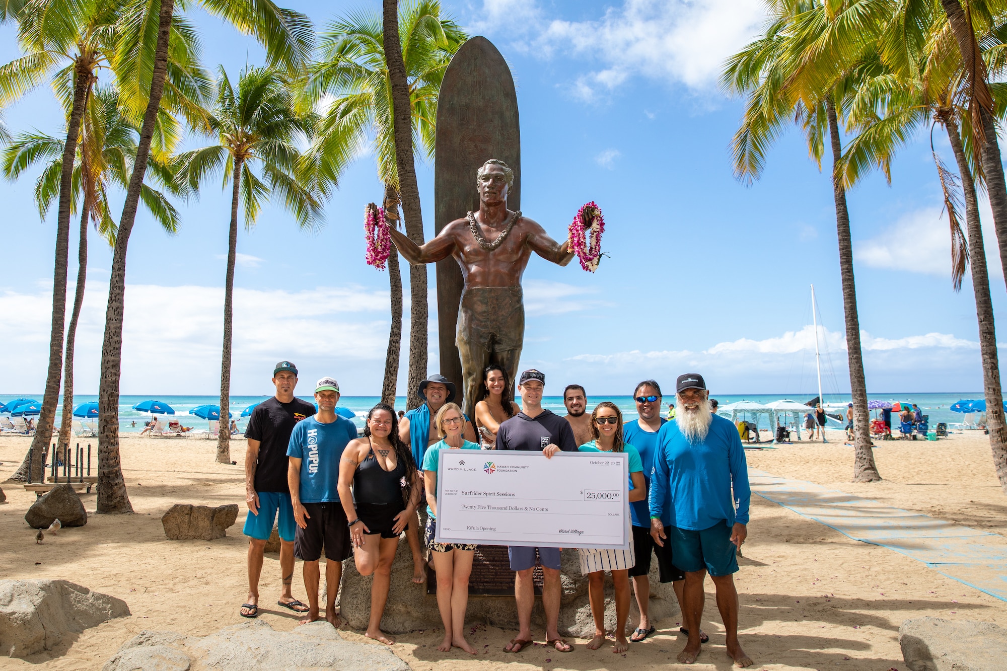 Group of people receiving a check donation in front of the Duke Kahanamoku statue.
