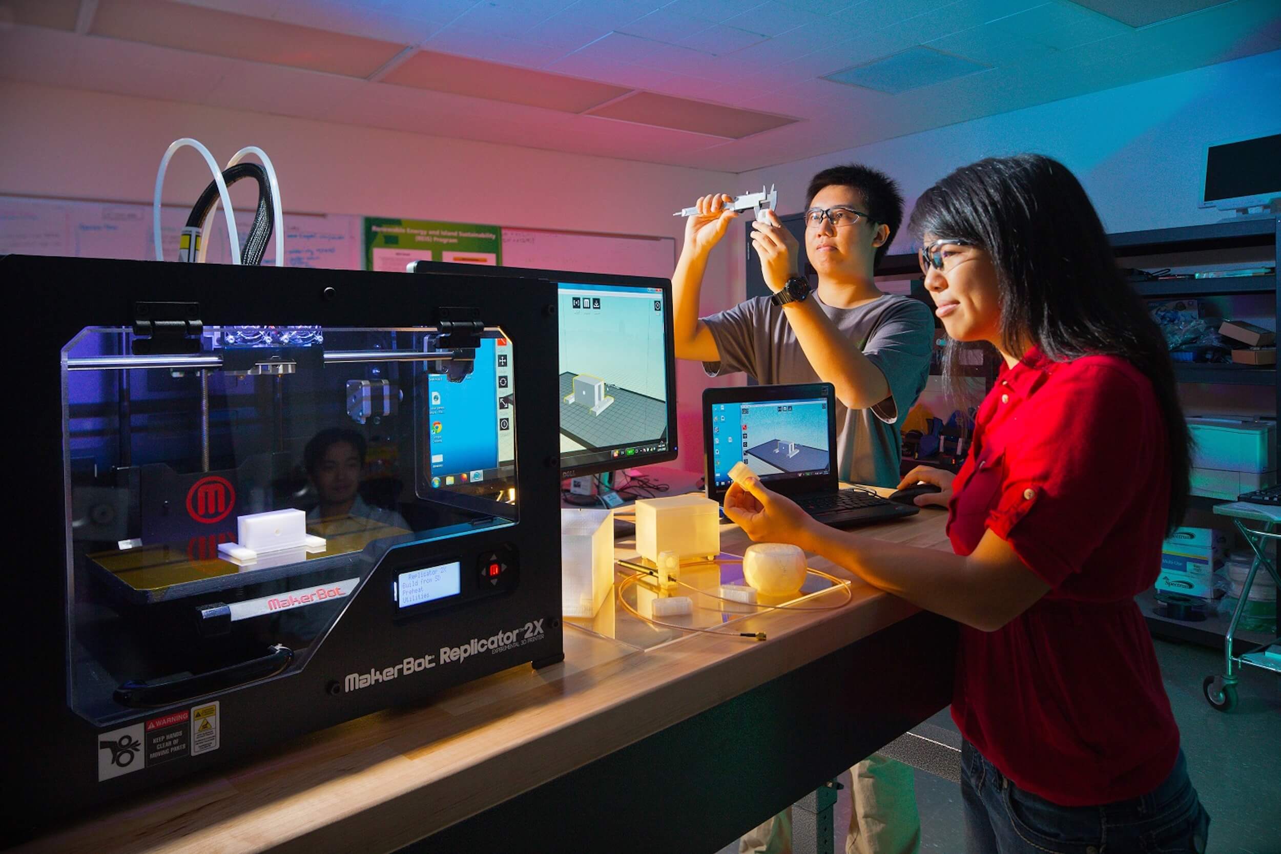 A man and woman studying equipment and computer monitors in an engineering lab.