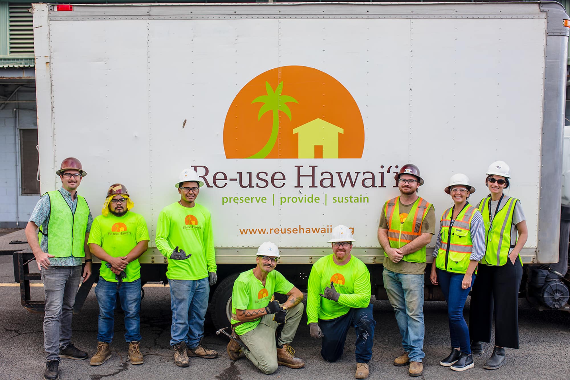 People wearing construction gear and hard hats posing in front of a large Re-use Hawaii cargo truck.