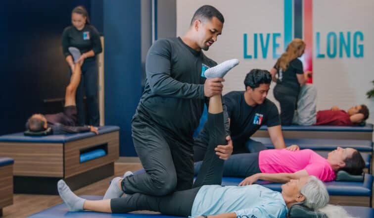 A stretch therapist assists a client lying on a table in a studio with others receiving similar sessions.